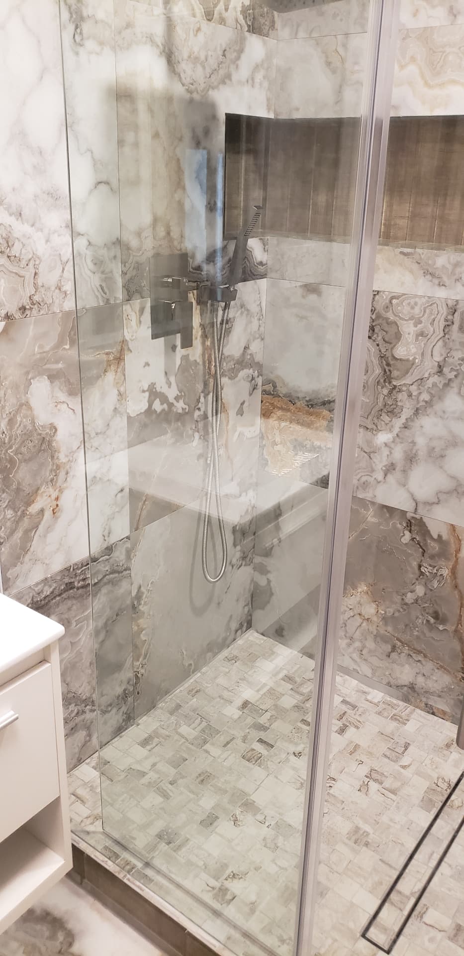 View through glass of a mosaic tiled shower floor and built-in bench