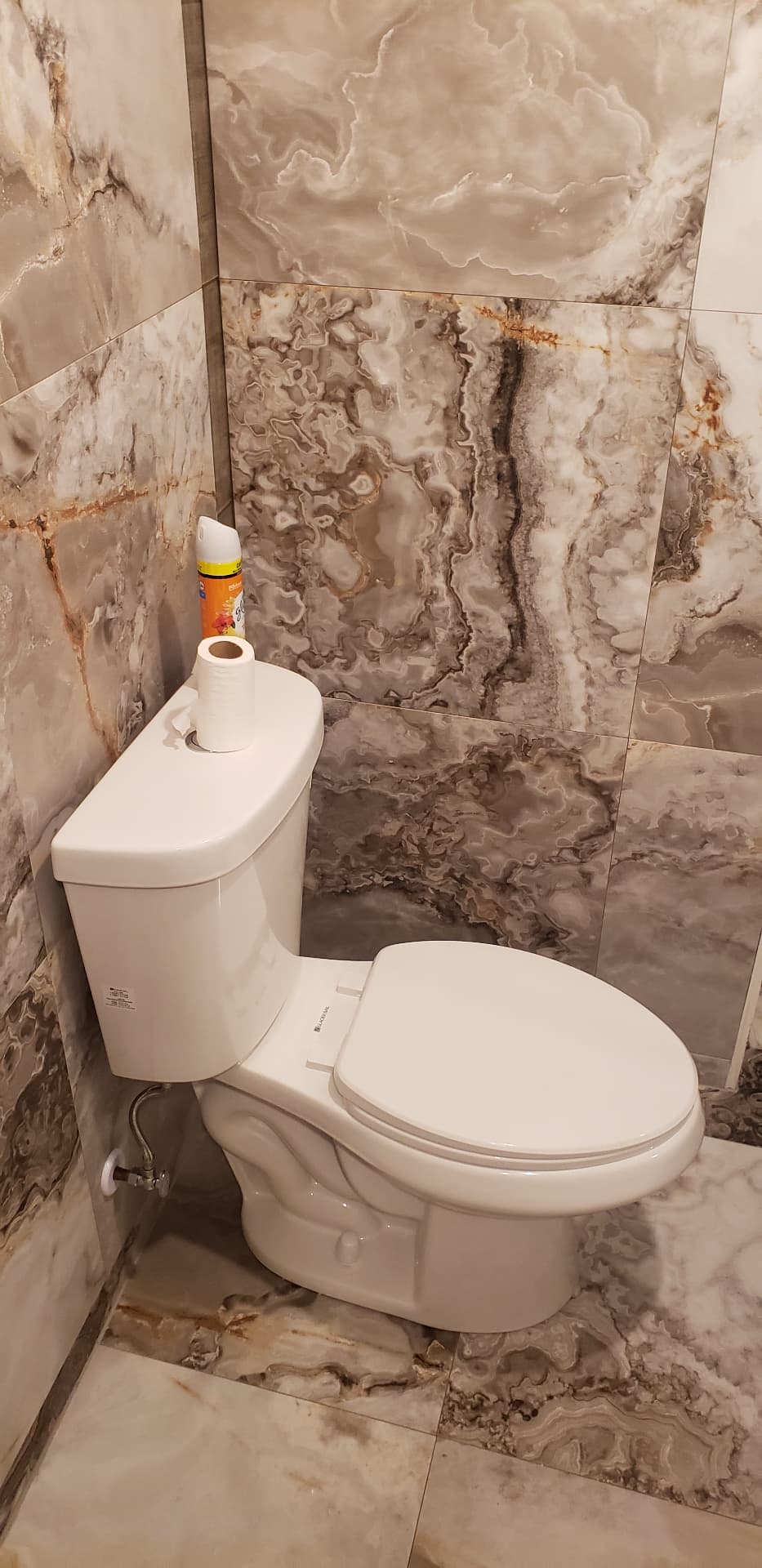Toilet installed in a corner surrounded by marble-look wall and floor tile