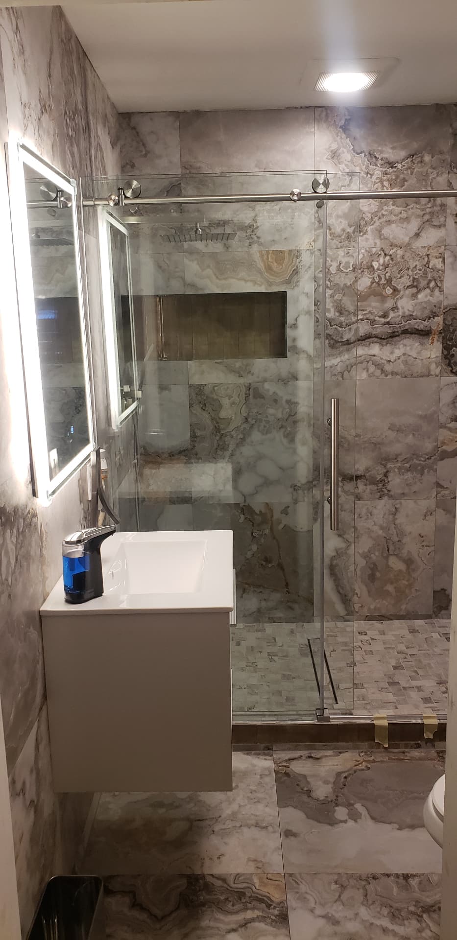 Finished bathroom remodel with marble-look tile, frameless glass shower, floating vanity, and recessed niche