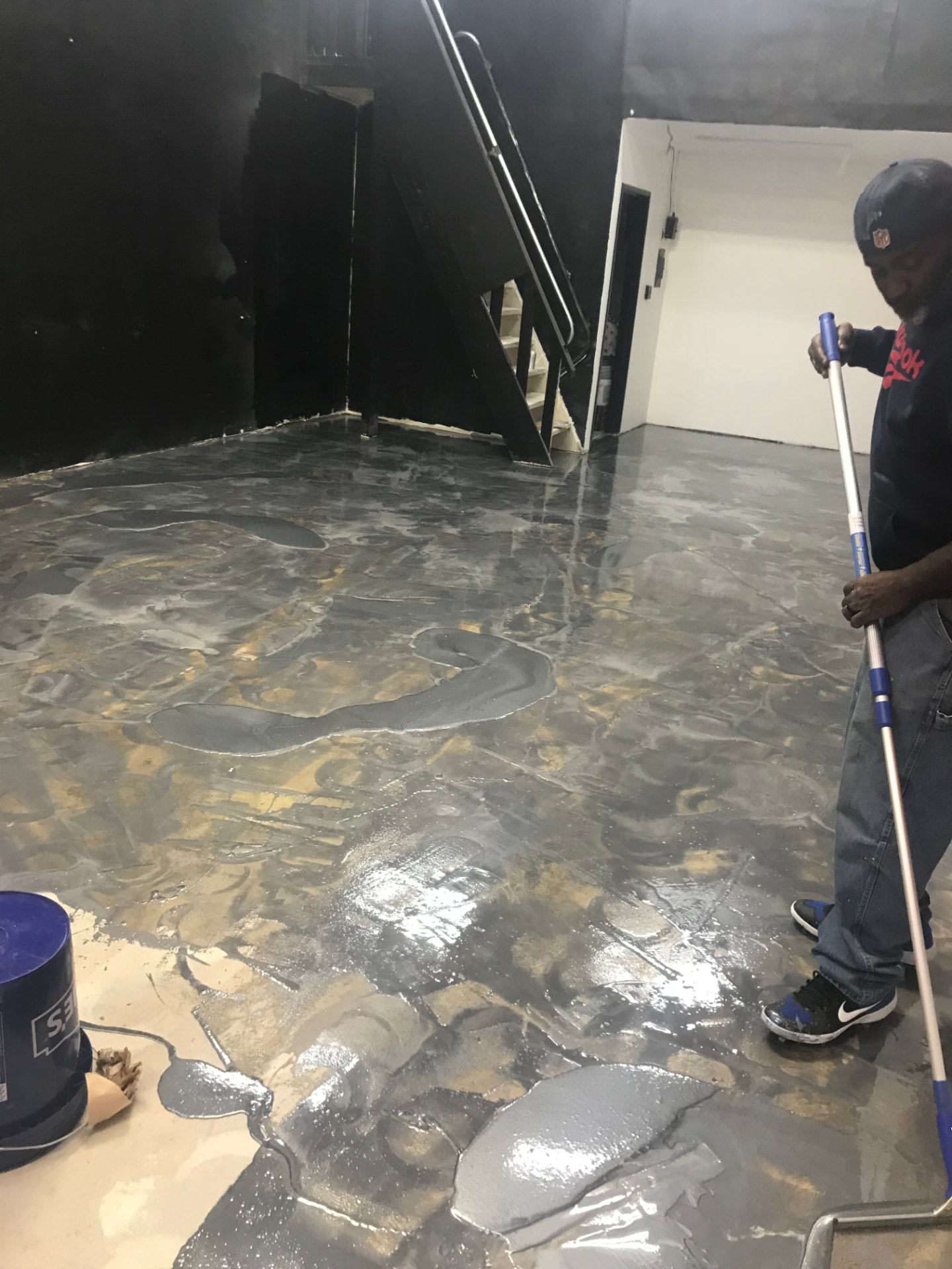 Installer spreading a wet gray metallic epoxy coating across a commercial floor