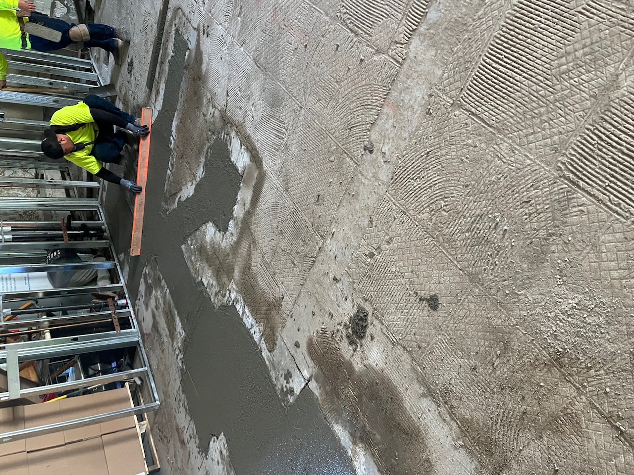 Worker screeding fresh concrete floor patch inside a commercial remodel