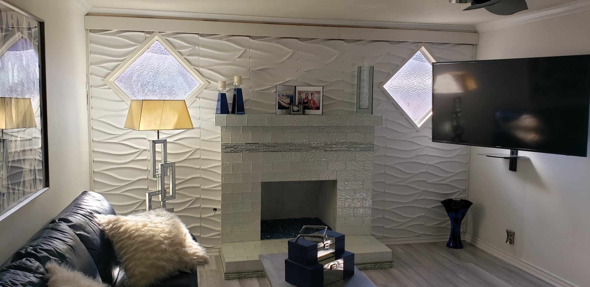 Finished living room restoration with a dimensional white feature wall, fireplace, and geometric windows