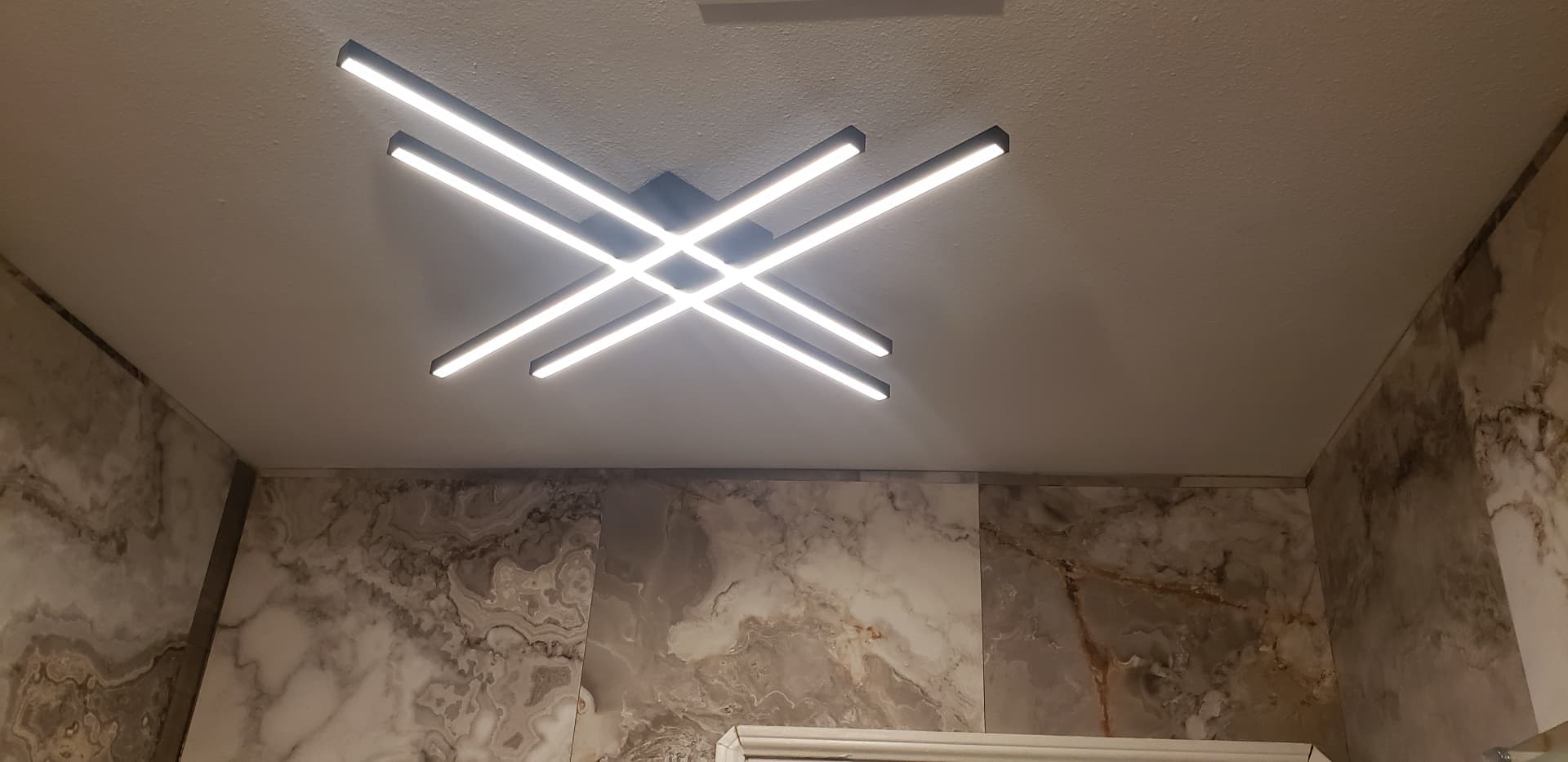 Crossed linear LED ceiling fixture above marble tiled bathroom walls