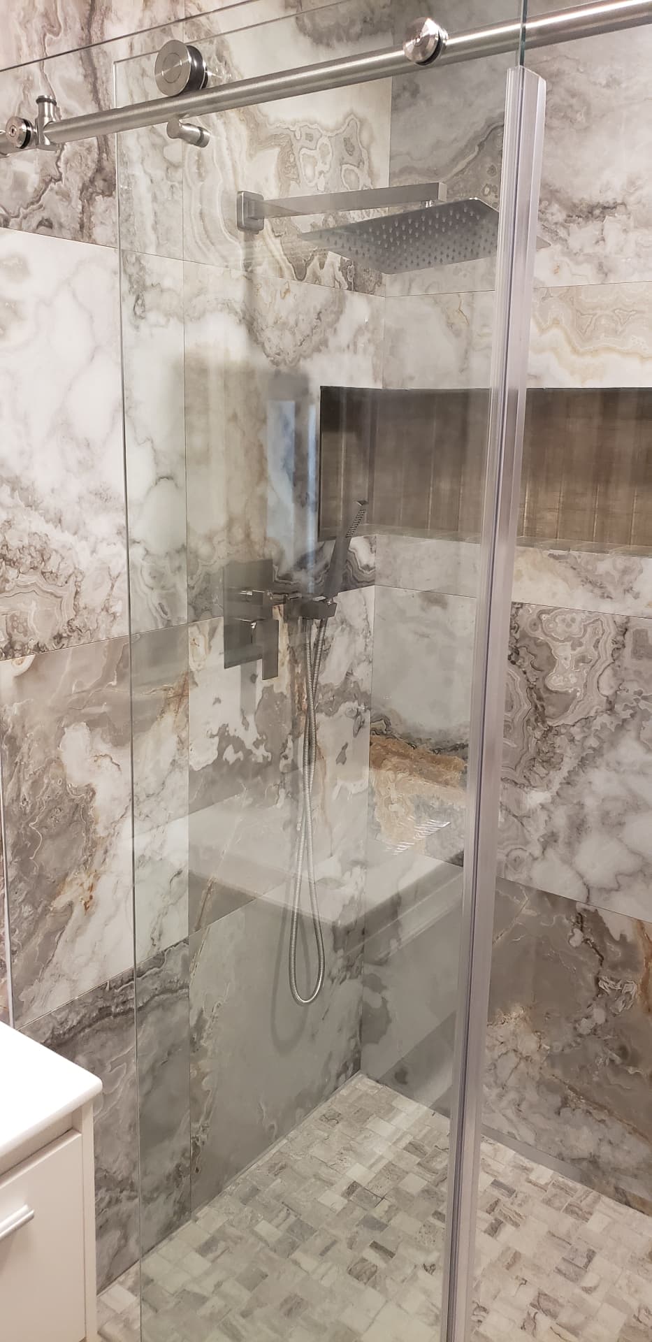 Frameless sliding glass shower door with brushed nickel rail and rollers