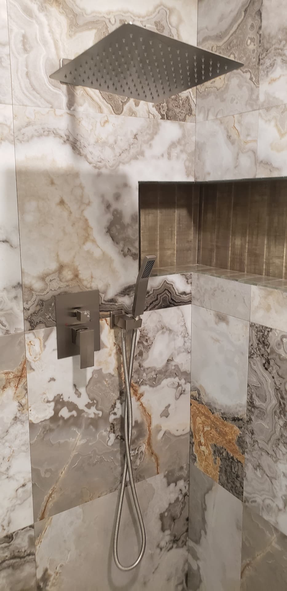 Shower control valve and handheld sprayer mounted on marble-look tile below a rain head
