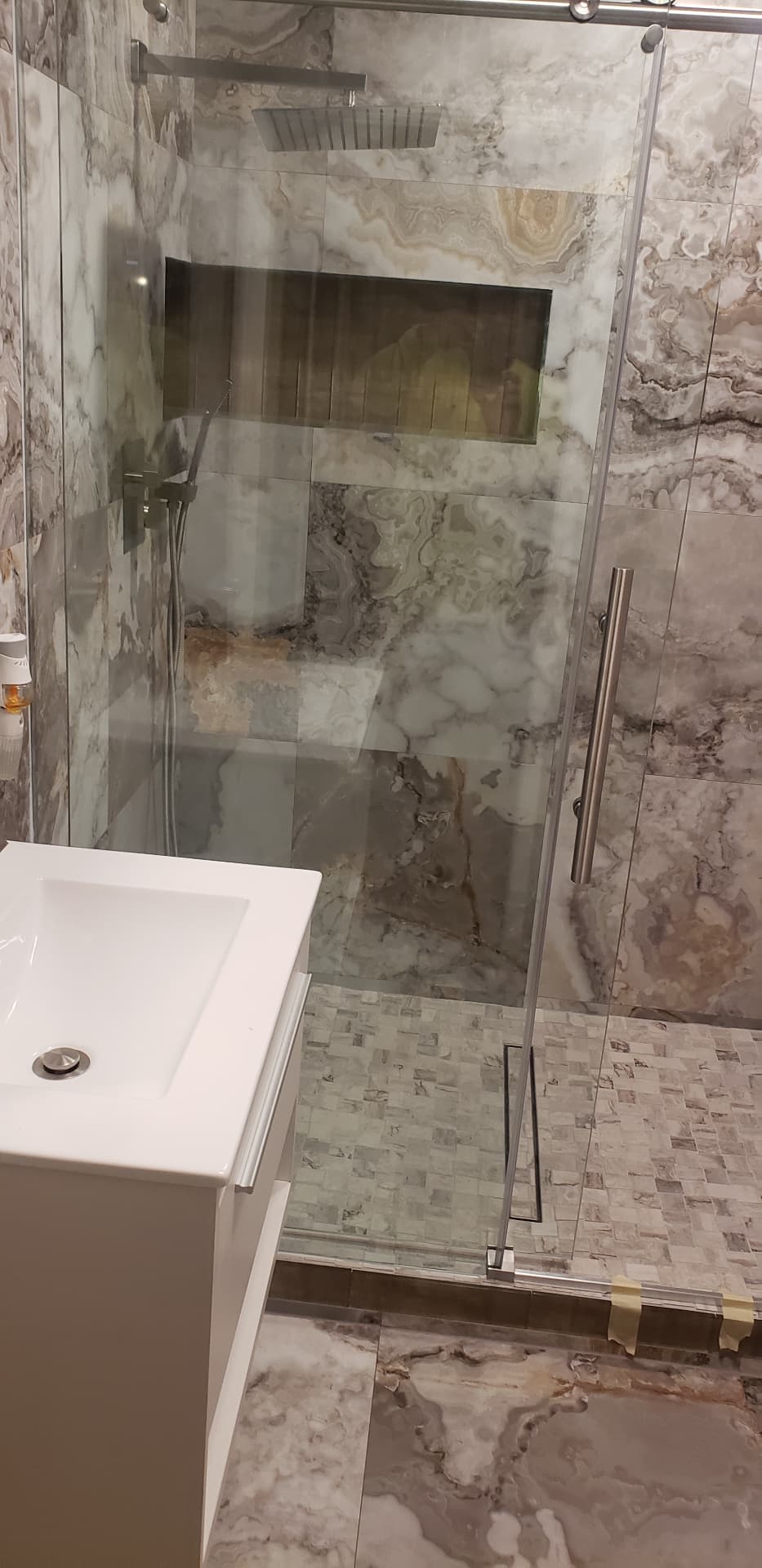 Floating white vanity next to a glass shower enclosure with marble-look tile