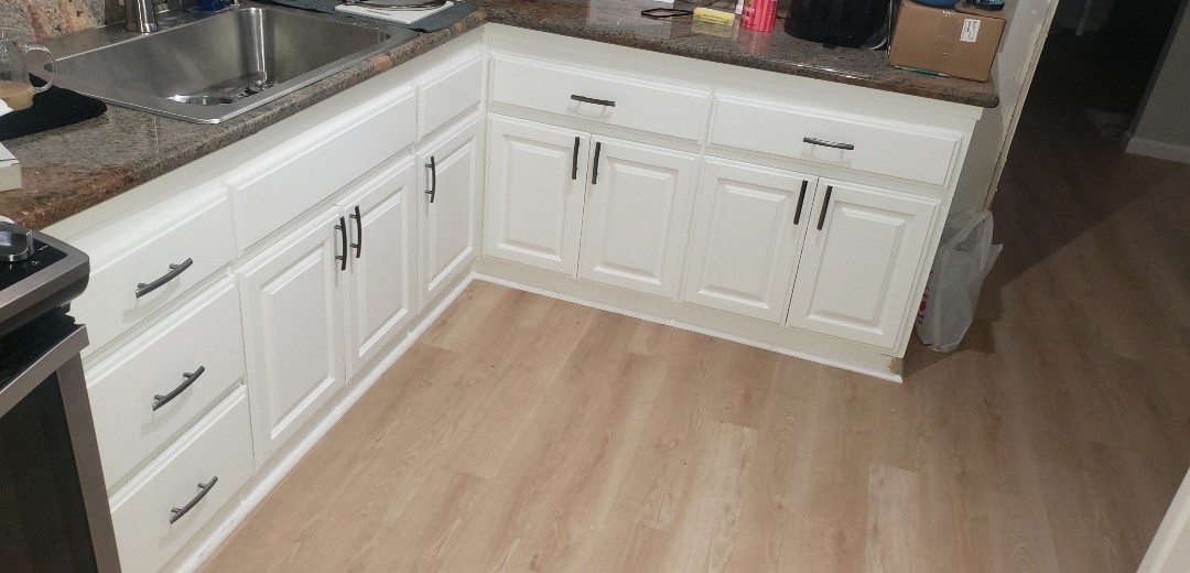 White resurfaced kitchen cabinets with granite countertop and new light wood-look flooring