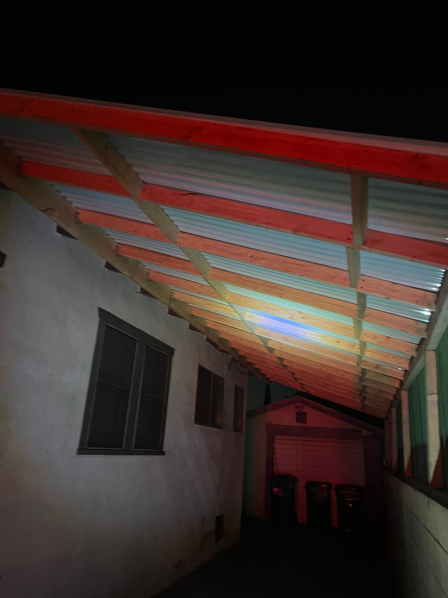 Covered side-yard patio with exposed wood rafters and translucent roof panels at night
