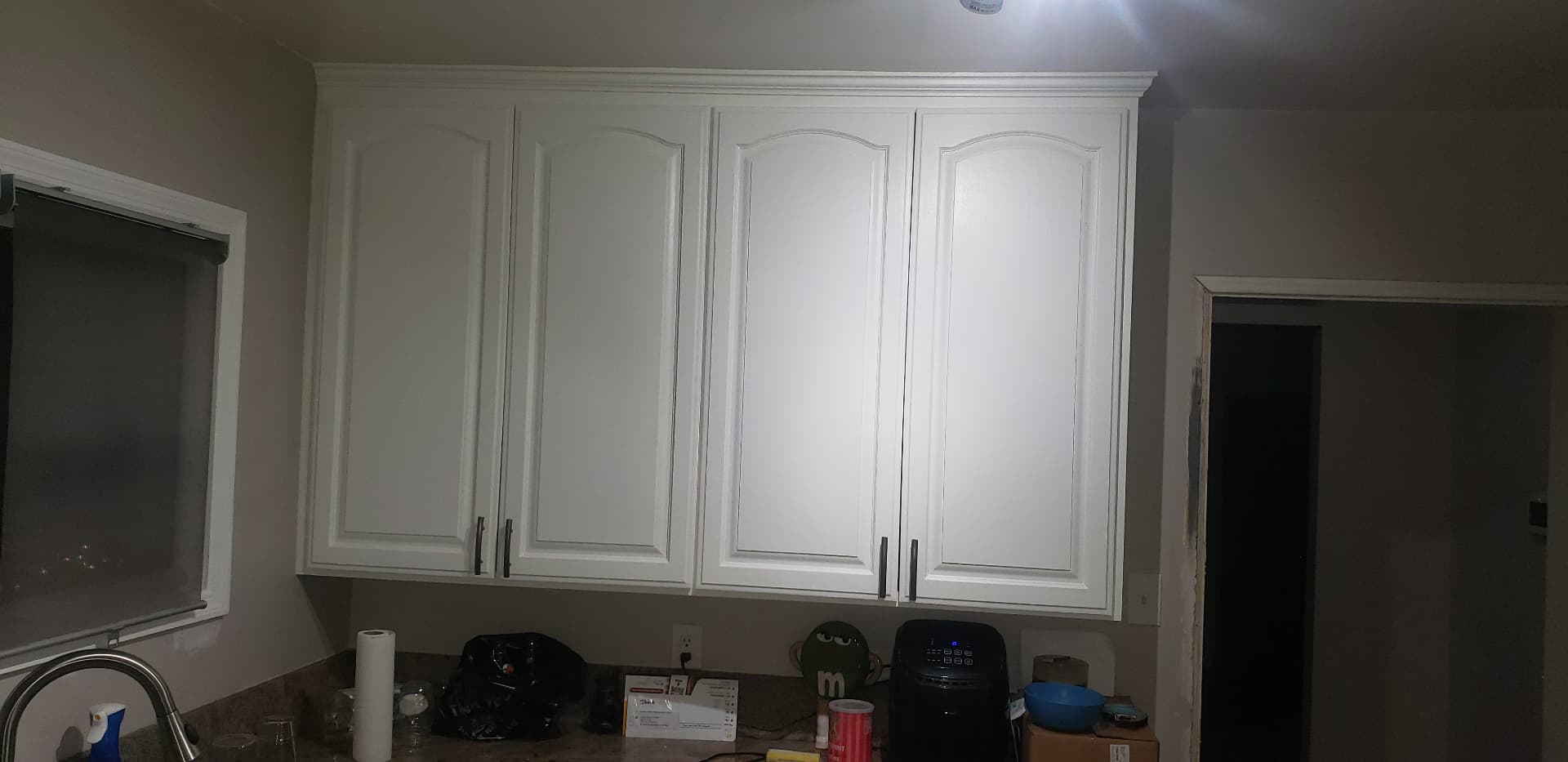 Resurfaced white upper kitchen cabinets with crown molding and dark pulls