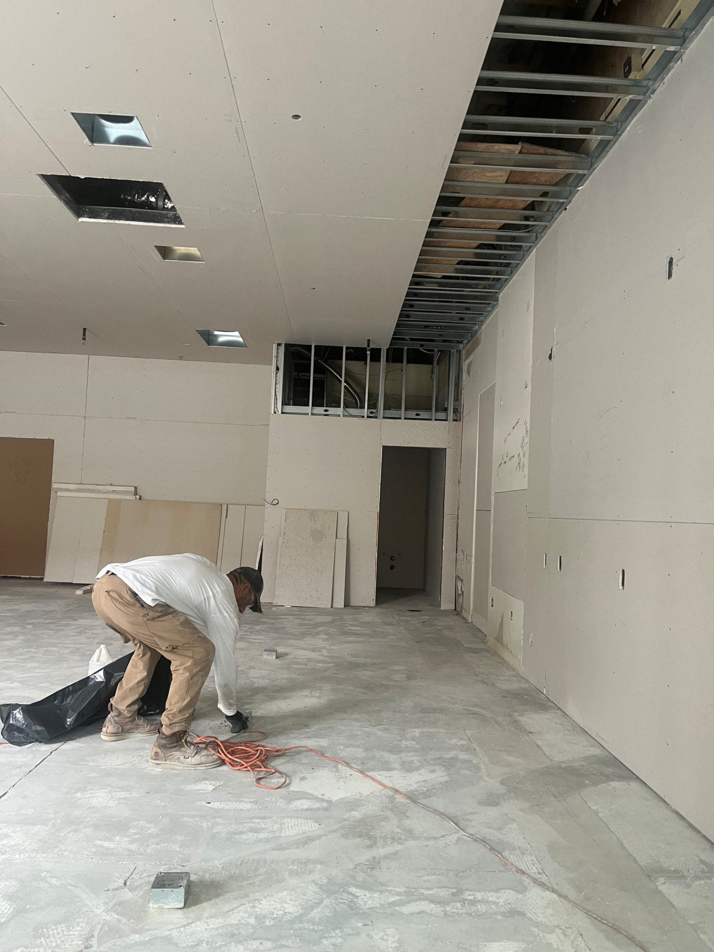 Worker hanging drywall in a commercial space with exposed steel ceiling framing