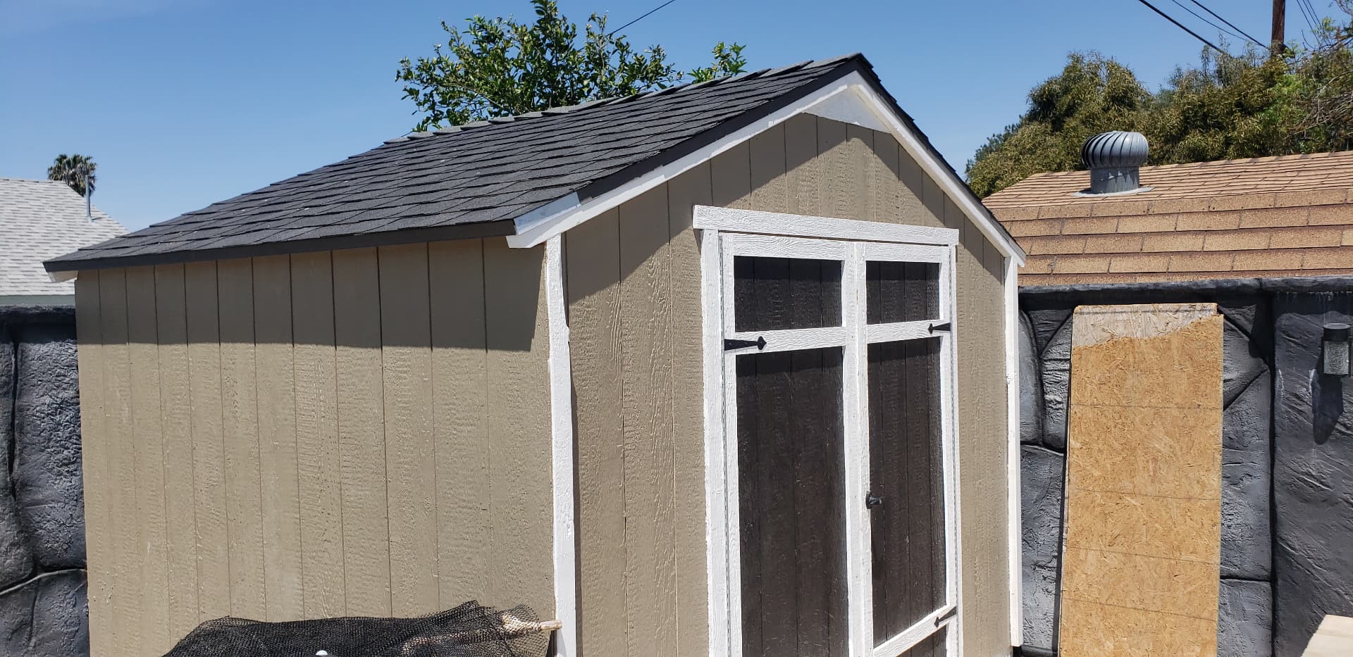 Finished backyard shed with a shingled roof, tan siding, and white trim