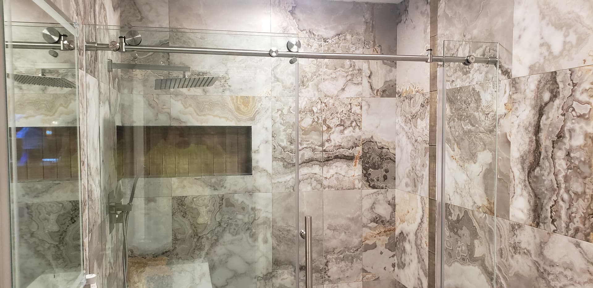 Wide view of a finished marble-look tile shower with sliding glass doors and lighted niche