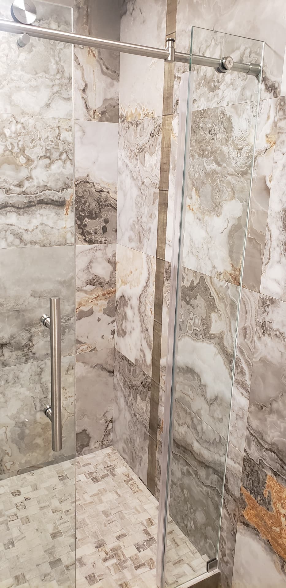 Sliding shower door handle and rail against marble-look tile with mosaic floor